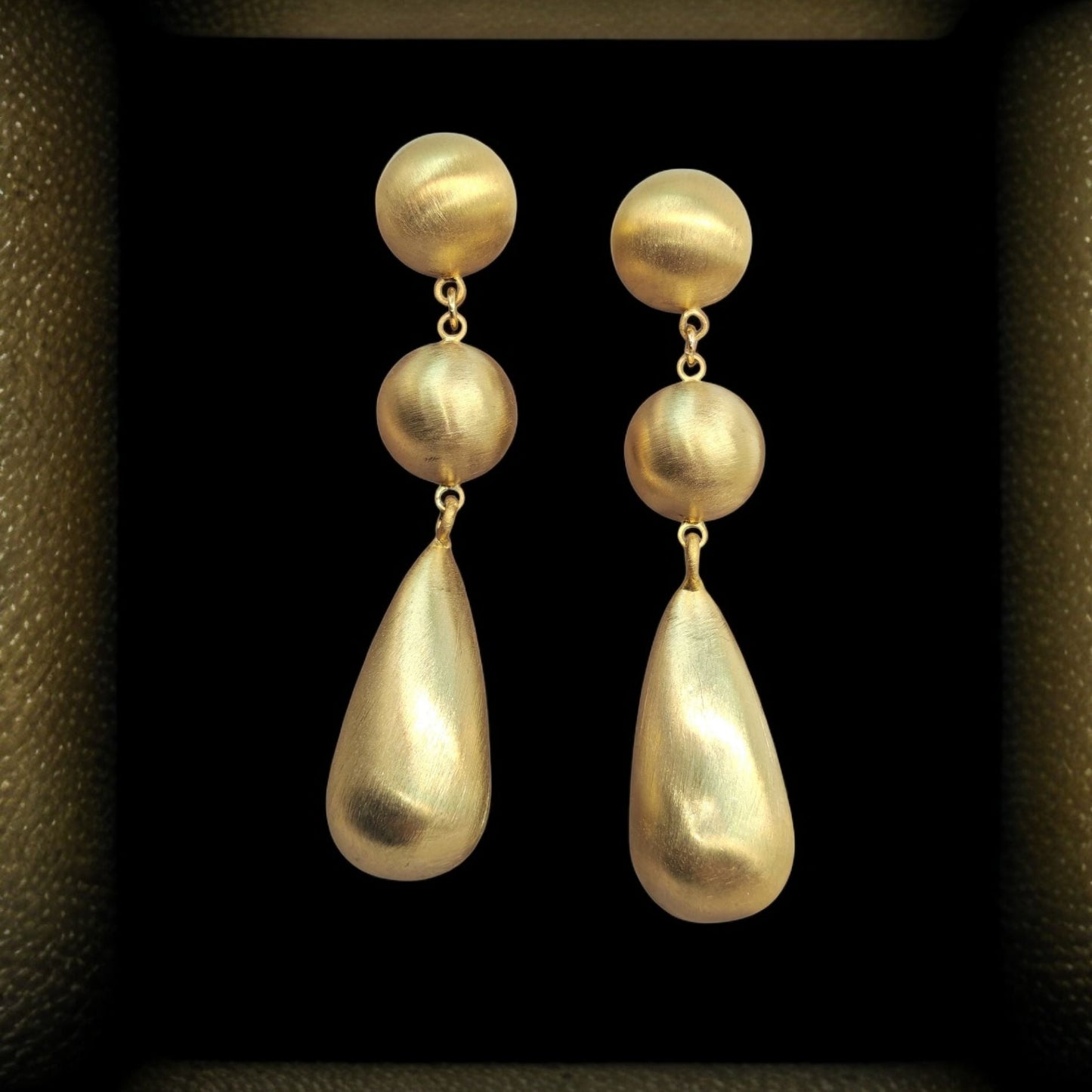 Pair of gold earrings with spherical and teardrop shapes on a dark background