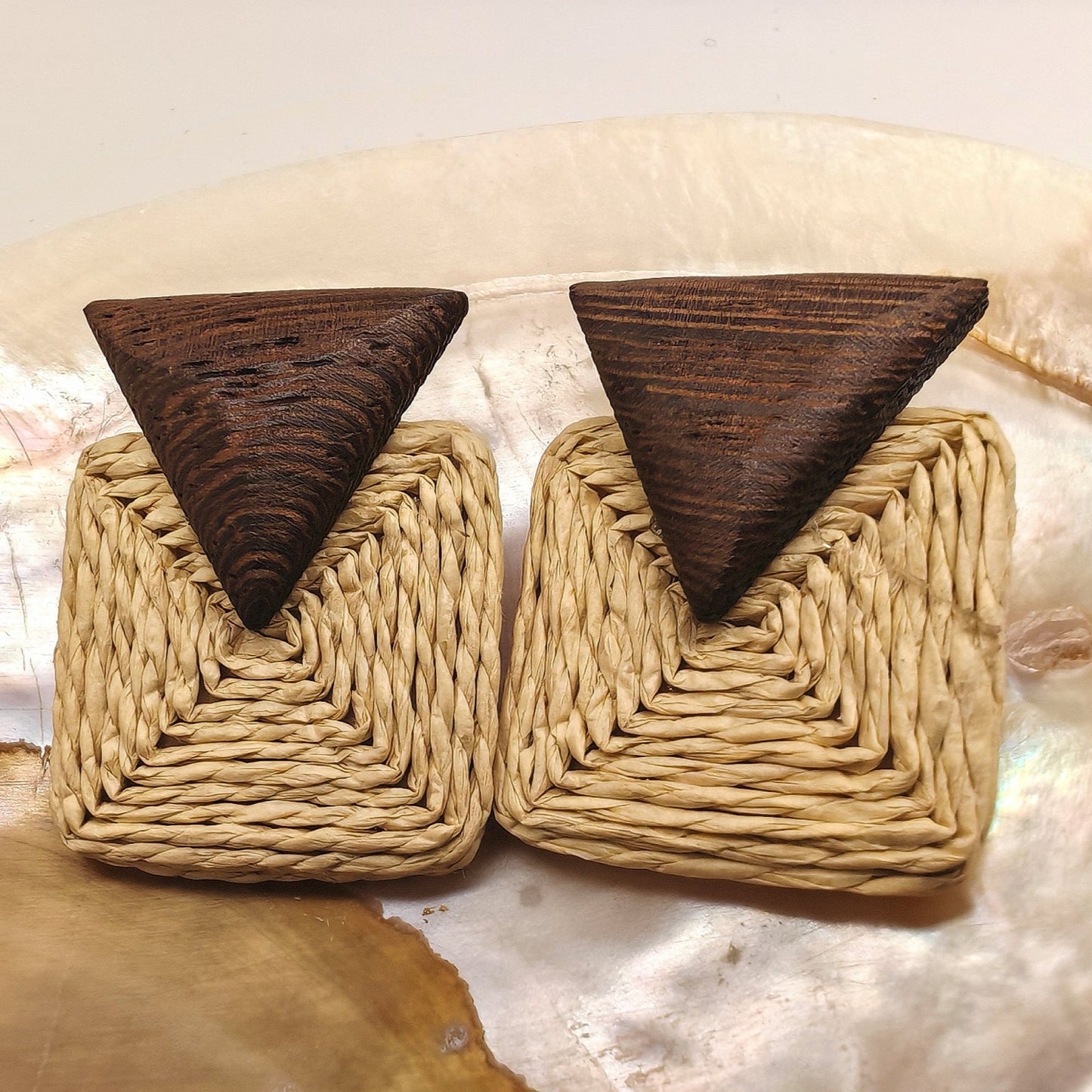 Pair of earrings with woven design and wooden triangle tops on a shell background