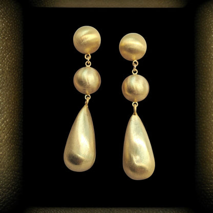 Pair of gold earrings with spherical and teardrop shapes on a dark background