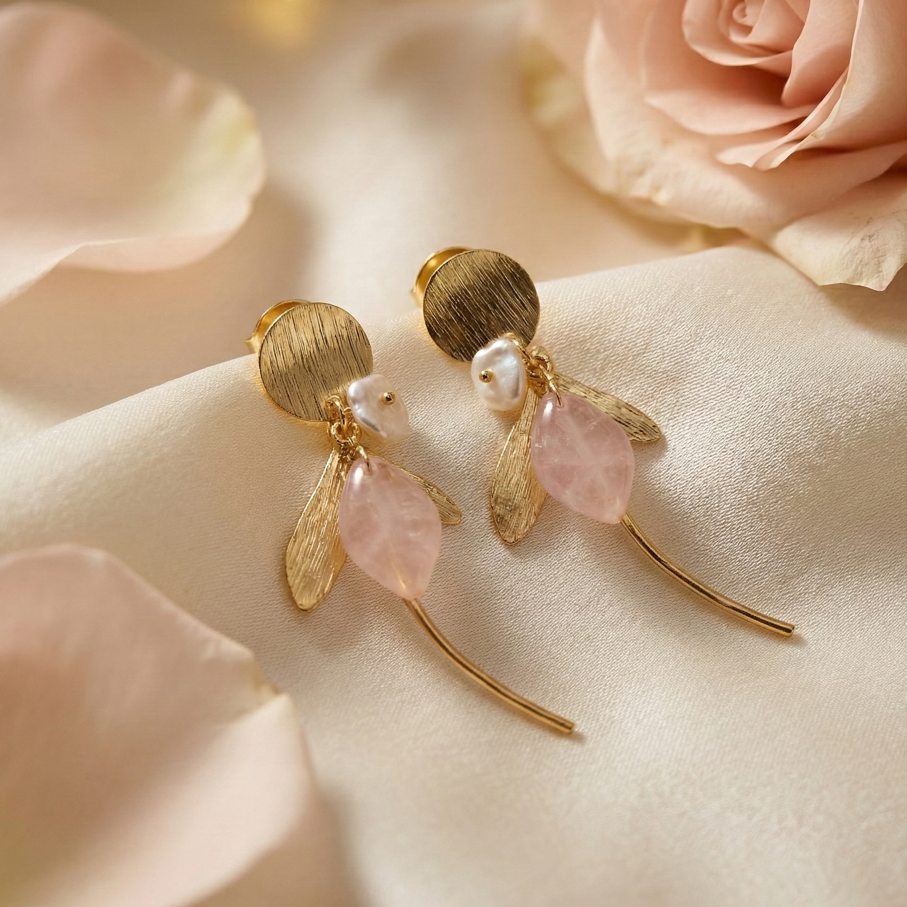 Gold earrings with pink stones on a soft pink fabric background