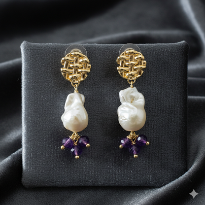 Pair of gold earrings with pearl and amethyst drops on a gray velvet stand.