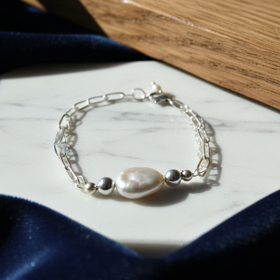 A silver-plated adjustable bracelet with a large, white baroque pearl pendant.
