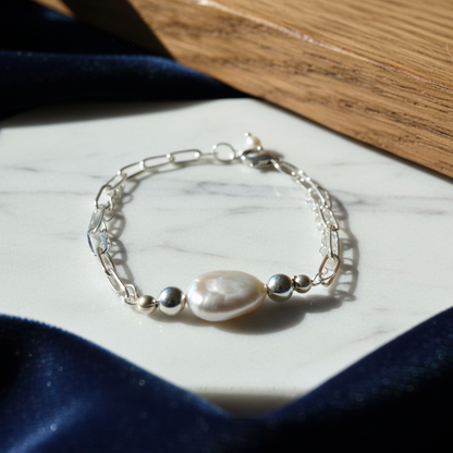 A silver-plated adjustable bracelet with a large, white baroque pearl pendant.