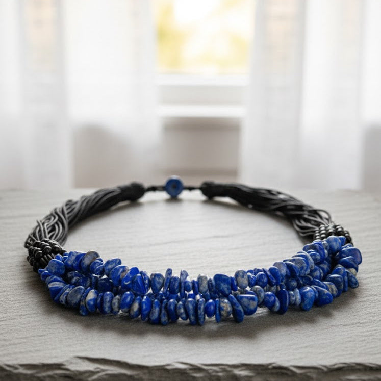 Necklace with blue beads and braided design on a wooden surface with a blurred window background