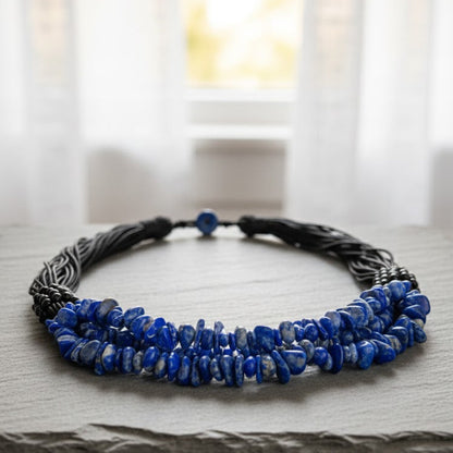 Necklace with blue beads and braided design on a wooden surface with a blurred window background
