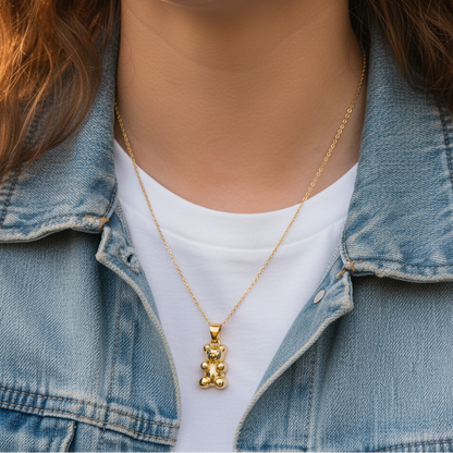 Person wearing a gold necklace with a teddy bear pendant, dressed in a denim jacket and white shirt.